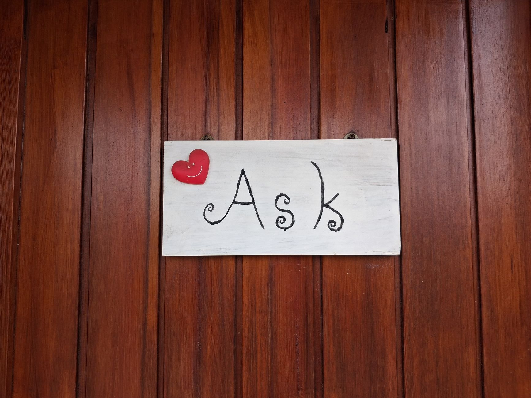 Rustic wooden wall with a decorative sign reading 'Ask' featuring a heart accent